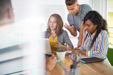 Multi ethnic group of succesful creative business people using a laptop during candid meeting-1
